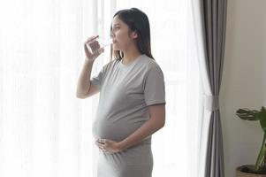Young pregnant woman drinking water at home, healthcare and pregnancy care concept photo