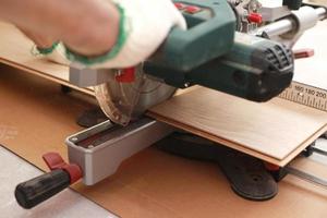 instalación de laminado o parquet en la habitación, el trabajador corta un laminado de cierta longitud con una sierra eléctrica. auto-reparación del piso en la casa foto