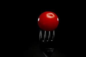 close up view of a fresh cherry tomato on fork isolated on a black background photo