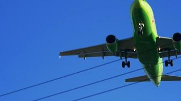 RUSSIA, MAY 26, 2021 Passenger airplane with flashing lights and airline logo takes off above high voltage lines against blue sky close low angle shot video