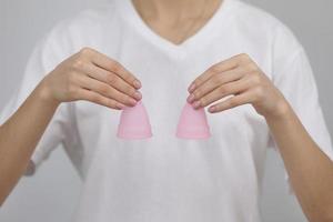 primer plano de una mujer sosteniendo copas menstruales rosas de diferentes tamaños en sus manos sobre fondo blanco. concepto de ginecología foto