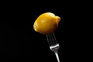 fresh lemon on the metal fork on a black background. Fresh tropical fruit, yellow citrus, flat layer, space for text photo