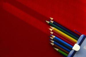 Multicolored pencils on a red background in the light photo