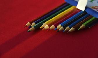 Multicolored pencils on a red background in the light photo