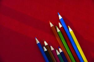 Multicolored pencils on a red background in the light photo
