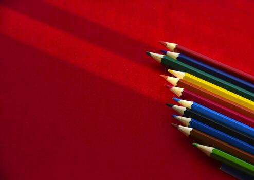 Multicolored pencils on a red background in the light photo