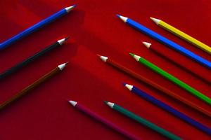 Multicolored pencils on a red background in the light photo