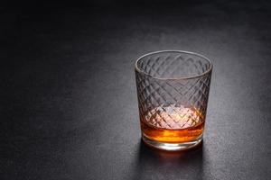 un vaso de whisky o coñac sobre una mesa de hormigón negro. tiempo de relajacion foto