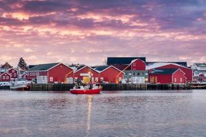 Beautiful rorbuer fishing village and fishing boat on coastline in the sunset at Reine town, Lofoten islands photo