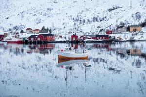 Fishing boat sailing reflection on arctic sea with scandinavian village photo