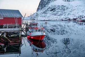 Fishing boat anchored on pier with red village in Lofoten islands photo