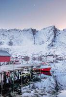 Red fishing boat anchored at pier with mountain reflection in arctic ocean