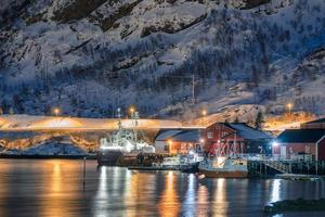 barco pesquero anclado en el muelle en un pueblo pesquero iluminado en la costa de las islas lofoten foto