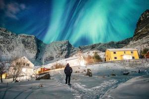 hombre turista de pie mirando la aurora boreal en el cielo en un pueblo de pescadores nevado foto