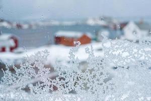 copo de nieve de primer plano en la ventana con casa borrosa en invierno