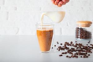 una mano anónima está vertiendo leche en un vaso de café de doble cara. foto