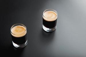 Vista detallada de primer plano de dos vasos de chupito espresso sobre un fondo negro brillante y elegante con espacio para copiar. foto