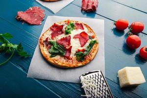 Top view of pizza over trendy blue wooden vintage backdrop with pizza ingredients. photo