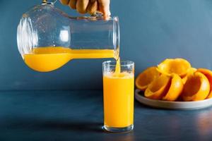 una mano anónima está llenando el vaso de jugo de naranja fresco foto