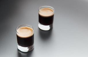 Closeup detail view of two espresso shot glass over shiny elegant black backdrop with copy space. photo