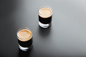 Vista detallada de primer plano de dos vasos de chupito espresso sobre un fondo negro brillante y elegante con espacio para copiar. foto