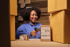 African American female worker in safety uniform using bar code scanner to check shipment orders at parcels warehouse, paper manufacture factory for the packing industry, logistic transport service. photo