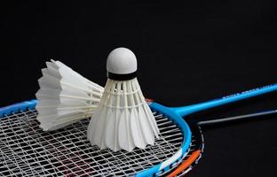 volante de bádminton blanco crema y raqueta con sombreado de luz de neón en el suelo verde en la cancha de bádminton interior, fondo de bádminton borroso, espacio para copiar. foto