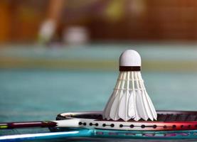 volante de bádminton blanco crema y raqueta con sombreado de luz de neón en el suelo verde en la cancha de bádminton interior, fondo de bádminton borroso, espacio para copiar. foto