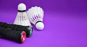 White cream badminton shuttlecocks and handles badminton rackets on purple floor, indoor badminton court, soft and selective focus on shuttlecock, concept for badminton sport lovers around the world. photo