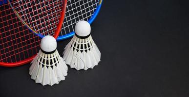 Cream white badminton shuttlecocks and rackets on black floor in indoor badminton court, copy space. photo