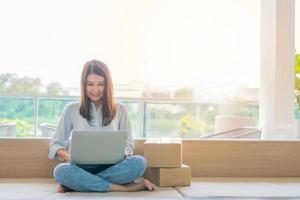 Happy young Asian woman entrepreneur, Smile for sales success after checking order from online shopping store in a laptop at home office, Concept of merchant business online and eCommerce photo
