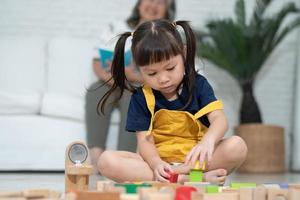 linda niña asiática jugando con coloridos bloques de juguete, los niños juegan con juguetes educativos en el jardín de infantes o en la guardería. juego creativo del concepto de desarrollo infantil, niño pequeño en la guardería. foto