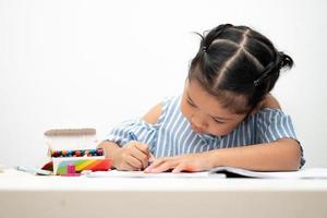 Cute adorable asian ethnic kid girl holding color pen drawing and painting on the table, She is Having Fun and Laughs. Concept of learn and enjoy creative hobby, child development. photo
