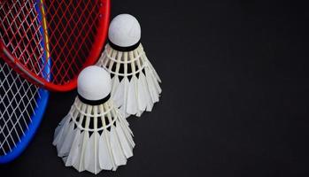 Cream white badminton shuttlecocks and rackets on black floor in indoor badminton court, copy space. photo