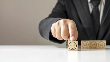 Hand holding Happy icon on a wooden cube block on the table, business annual satisfaction survey concept. photo