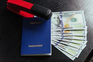 Top view of passport with dollar bills and stapler on wooden table. photo