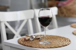 a glass of wine and some wine tools on a white wooden surface. Red wine photo