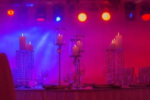 Festive table decorated with composition of candles and silver candlesticks in colored light in the banquet hall. Table newlyweds in the banquet area on wedding party. photo