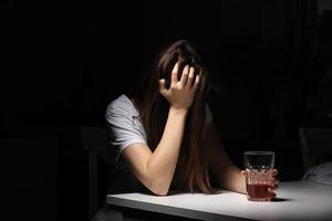 Close up of woman sitting and holds glass with whiskey or cognac having alcohol addiction, depressed female drinking strong alcohol suffering from personal relationships problems photo