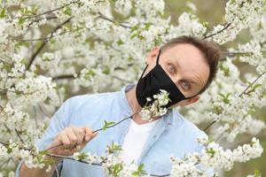 man in mask among flowering trees. man in a medical mask among a blossoming spring garden. Self-isolation and quarantine. cheerful man rejoices in the end of the pandemic and enjoys the spring. photo