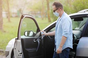 Spraying antibacterial sanitizer spray on car, infection control concept. Prevent Coronavirus, COVID-19, flu. Man wearing in medical protective mask driving a car. Disinfecting wipes. photo