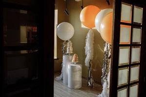 decoración para el primer cumpleaños con pastel de dos pisos y grandes globos blancos y beige con oropel. barra de caramelo con macarrones o macarons. fiesta de cumpleaños. enfoque selectivo foto