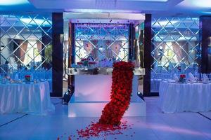 Festive table, arch, stands decorated with composition of red flowers and greenery, candles and mirrors in the banquet hall. Table newlyweds in the banquet area on wedding party.
