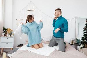 happy stylish loving couple having a pillow fight in bed. young man and woman expecting baby for Christmas. Selective focus photo