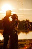 silueta de pareja amorosa abrazándose en el lago al atardecer. hermosa joven pareja enamorada caminando por la orilla del lago al atardecer en los rayos de luz brillante. copie el espacio enfoque selectivo foto