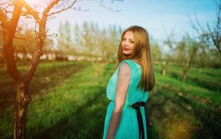 mujer con un hermoso vestido largo turquesa posando en un prado en el jardín de frutas. foto