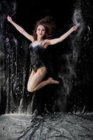 Girl dancer jumping and dancing in the white dust with flour on a black background. Studio shot of woman dancing with flour.