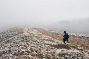 Tourist photographer with tripod on hand walking on frozen hill with fog. photo