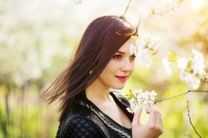 Cierra el retrato de una joven morena con flor de cerezo en el jardín de primavera. foto
