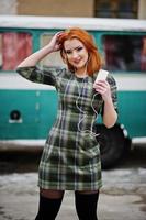 Young red haired girl lady with mobile cell phone and headphones, wearing on checked dress background old vintage turqoise minivan bus. photo